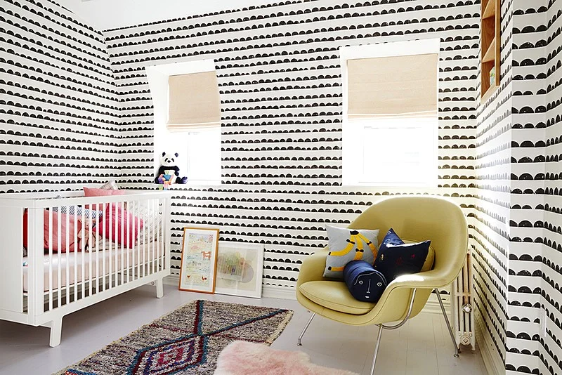 A nursery with bold black-and-white patterned walls includes a white crib and a yellow lounge chair.
