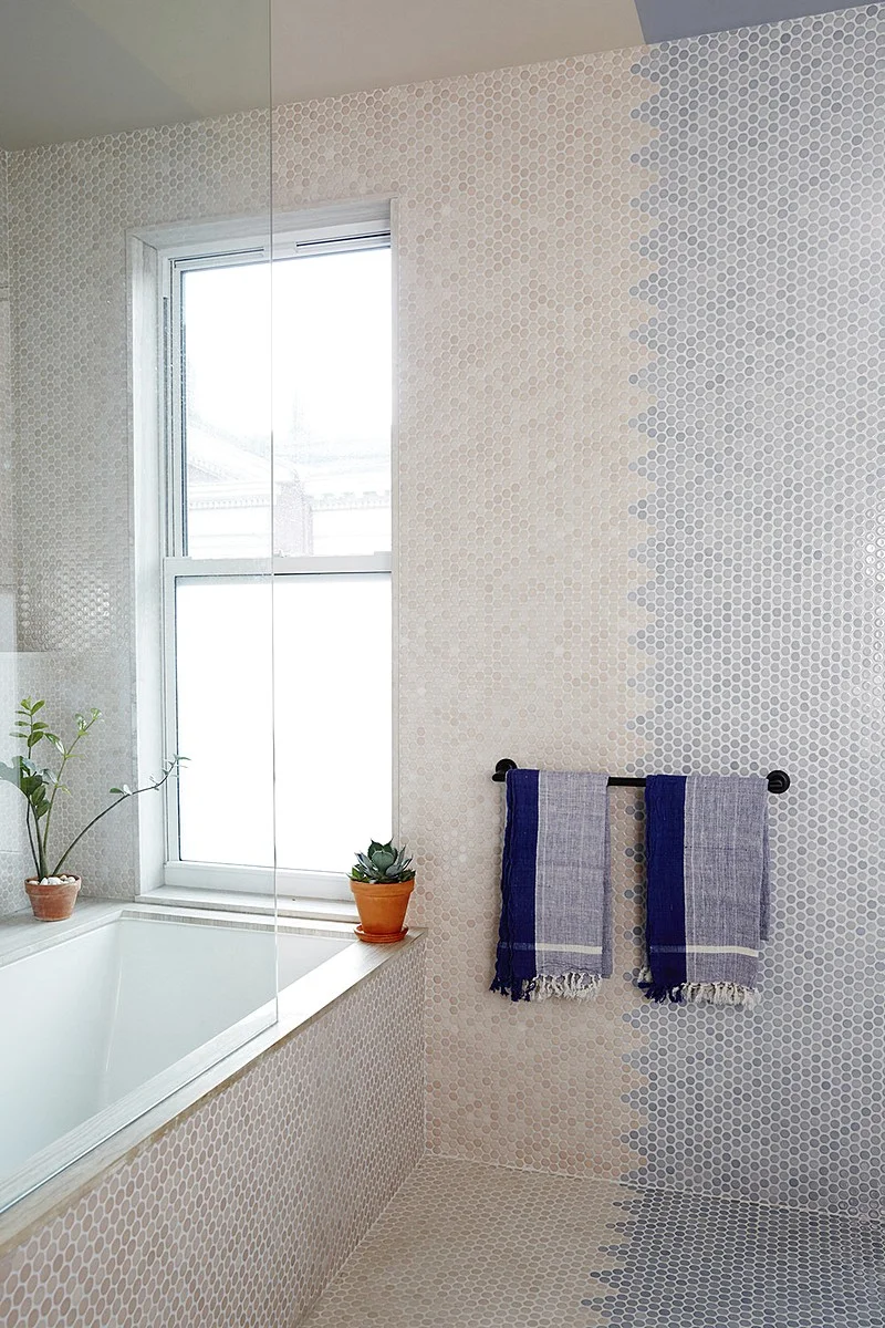 A built-in tub and towel bar sit against two-tone penny tile blending blush and slate blue.