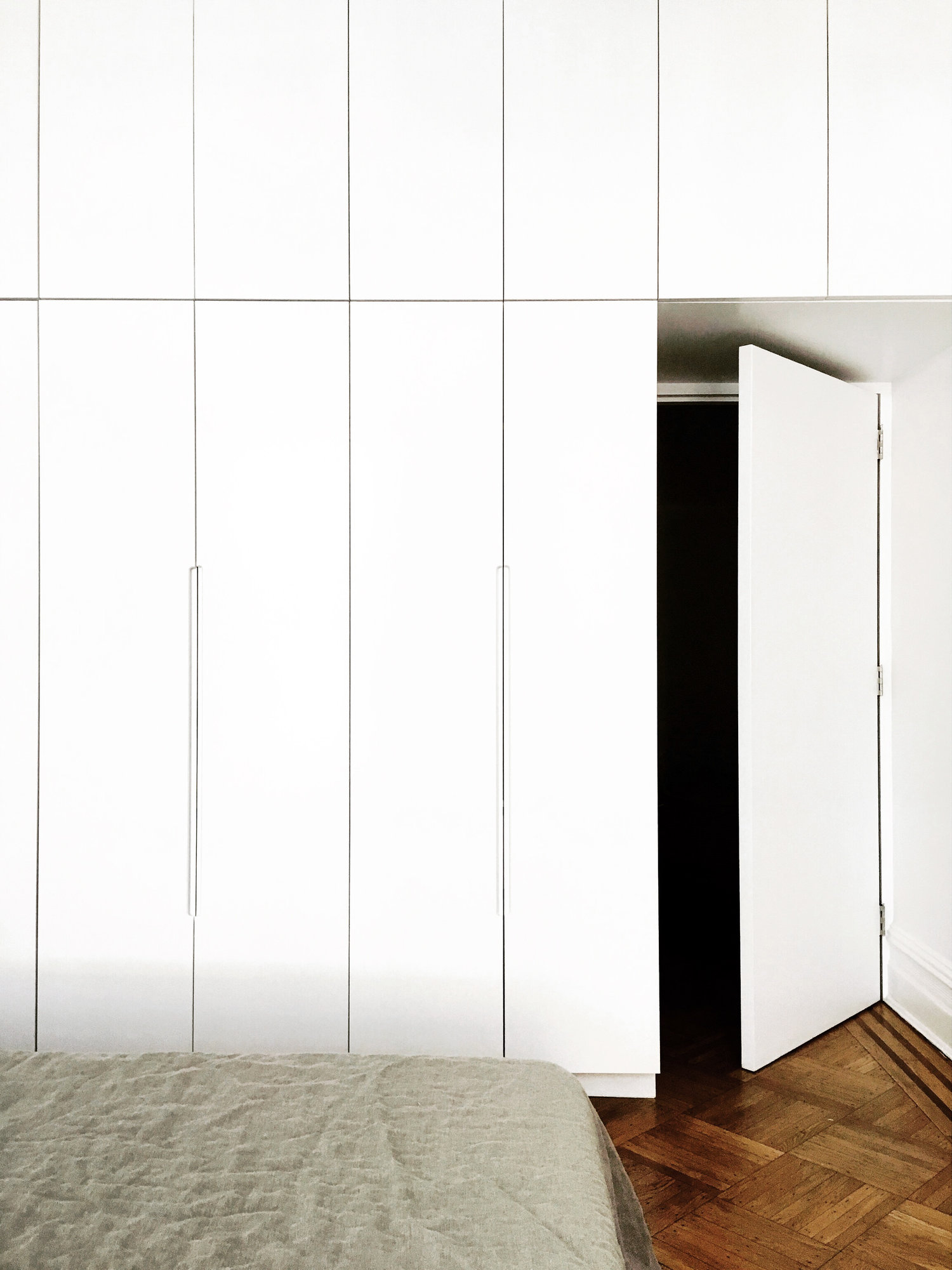 Floor-to-ceiling white wardrobes line the bedroom wall beside an open white door and restored parquet floor border.
