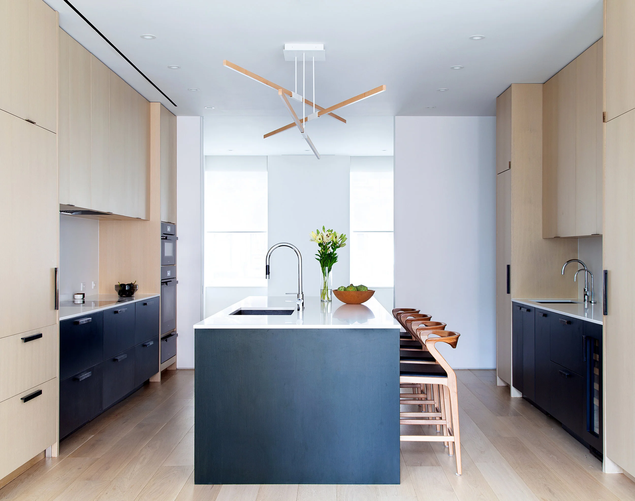 The galley kitchen pairs rift-cut white-oak millwork with black lower cabinets and a dark island lined with wood bar stools.