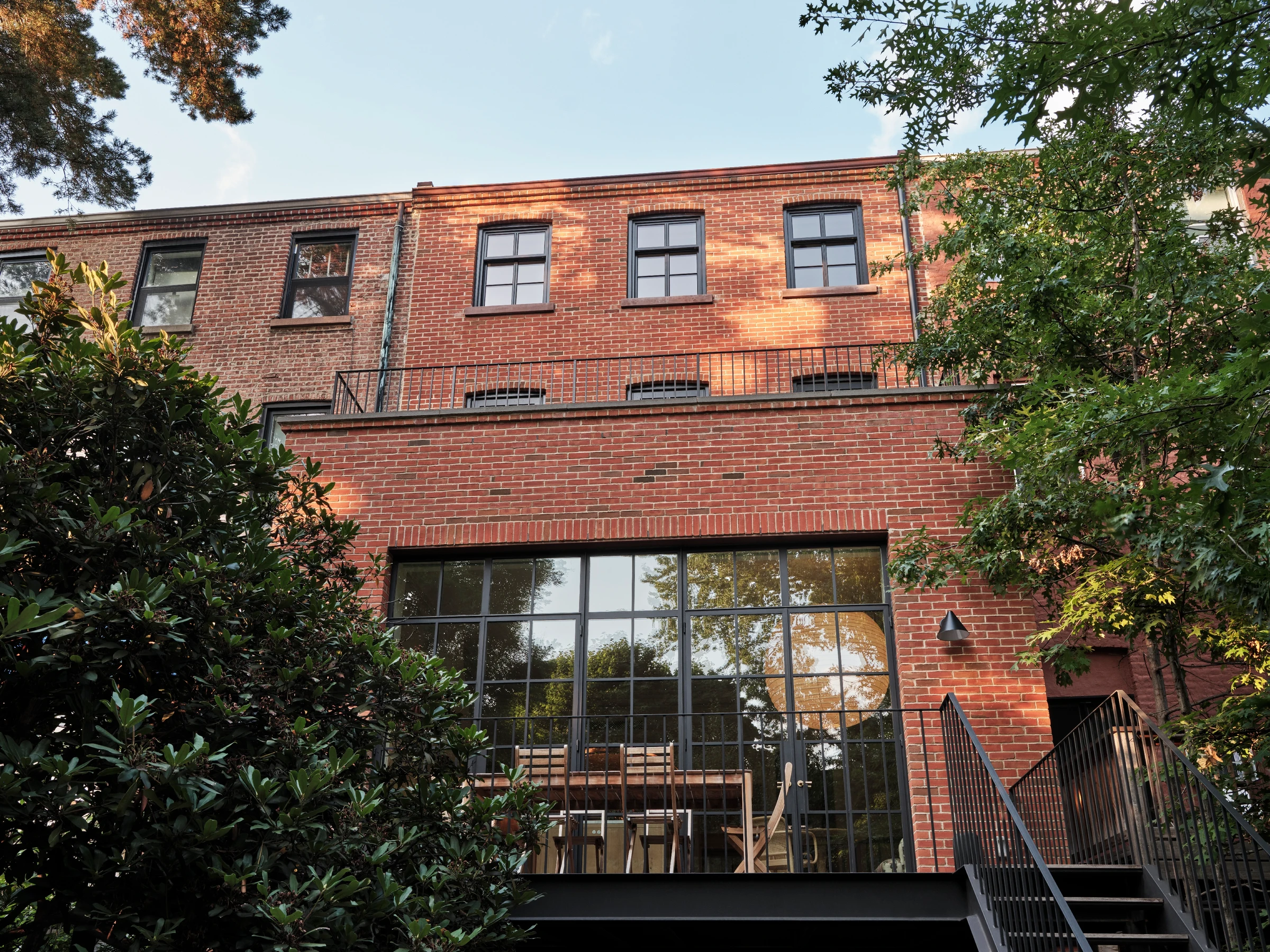 The rear terrace extends the full-width addition outdoors, using black steel and planting to connect the main rooms to the garden.