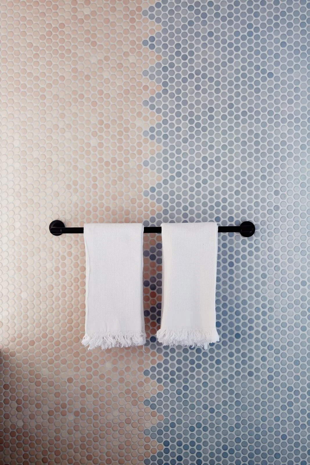 A close-up of the towel bar emphasizes the soft color transition across small round mosaic tiles.