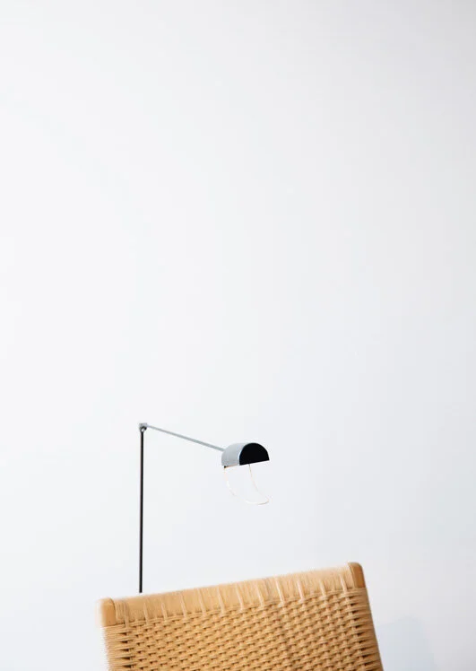 Only a black articulated wall lamp and the woven chair back interrupt this cool white plaster wall.