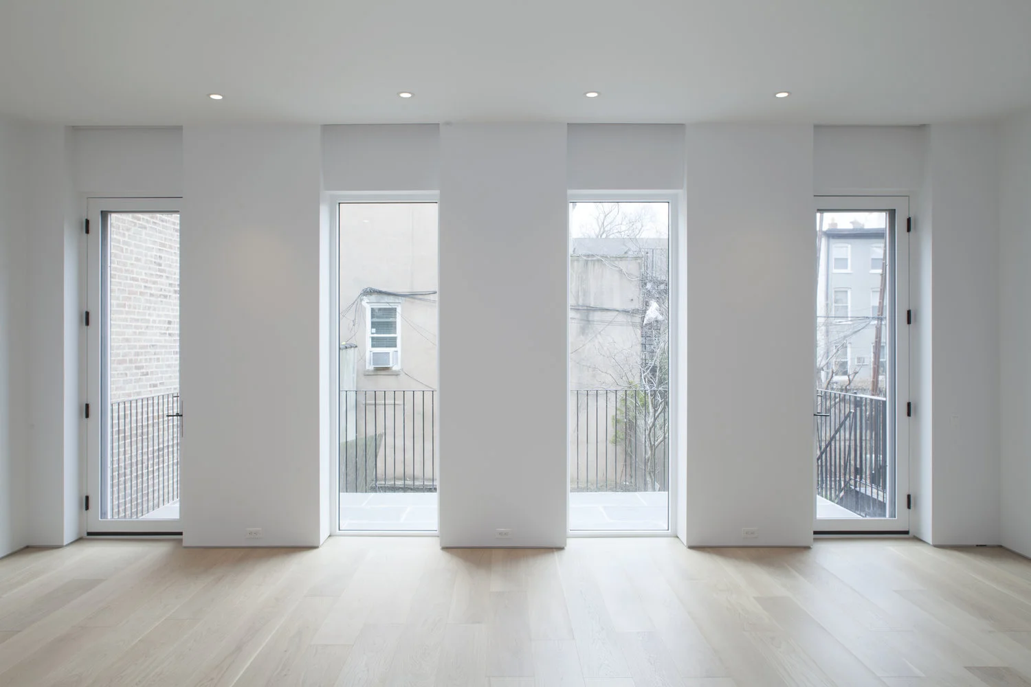 An empty rear room is defined by three full-height glazed openings and continuous wide-plank white-oak flooring.