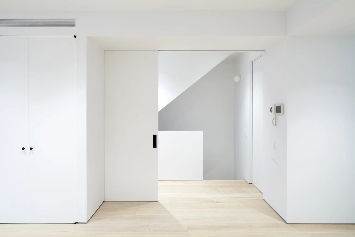 A full-height sliding pocket door aligns with flush closet fronts and a continuous white-oak floor plane.