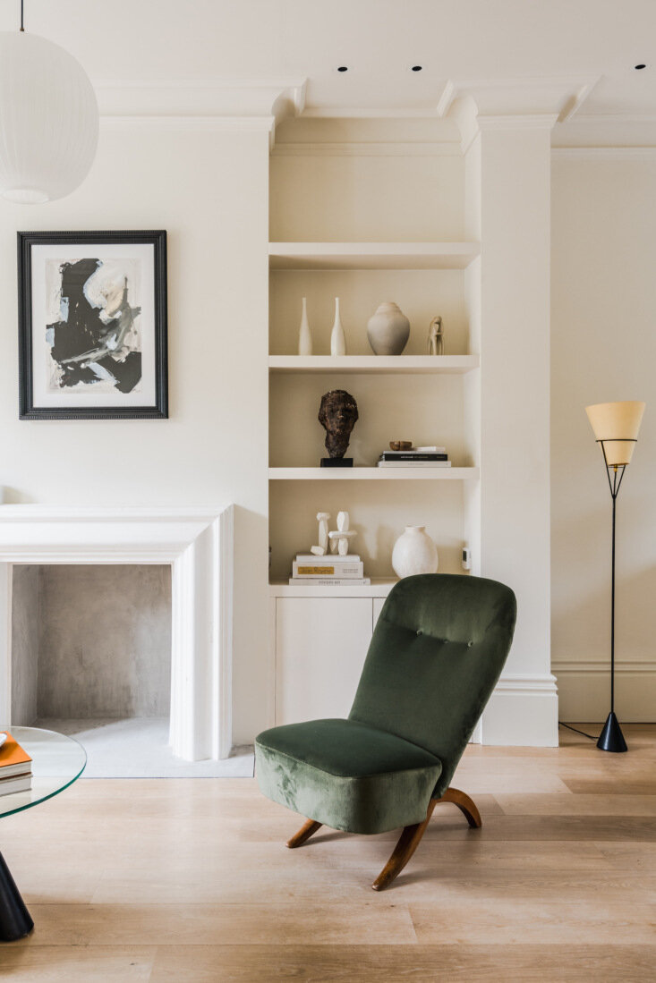 Front reception room anchors a 1950s Theo Ruth Congo chair in deep green upholstery beside built-in shelving and a simple mantel.