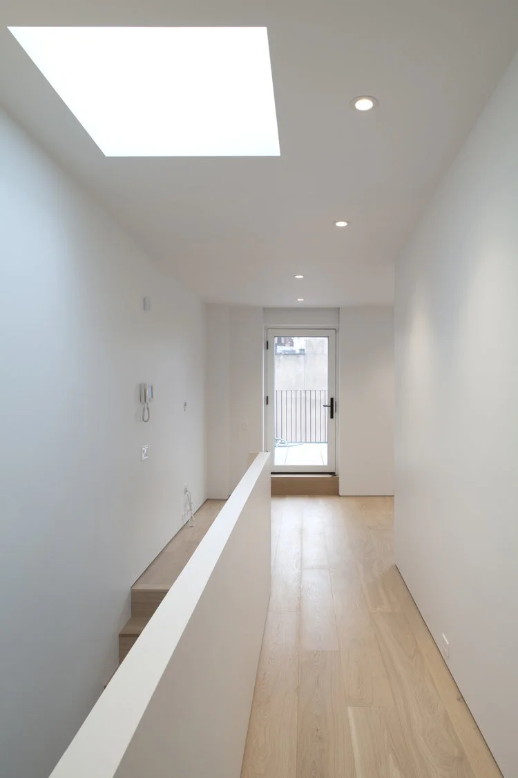 A skylit corridor runs above the stair with recessed downlights and a glazed door opening to a small terrace.