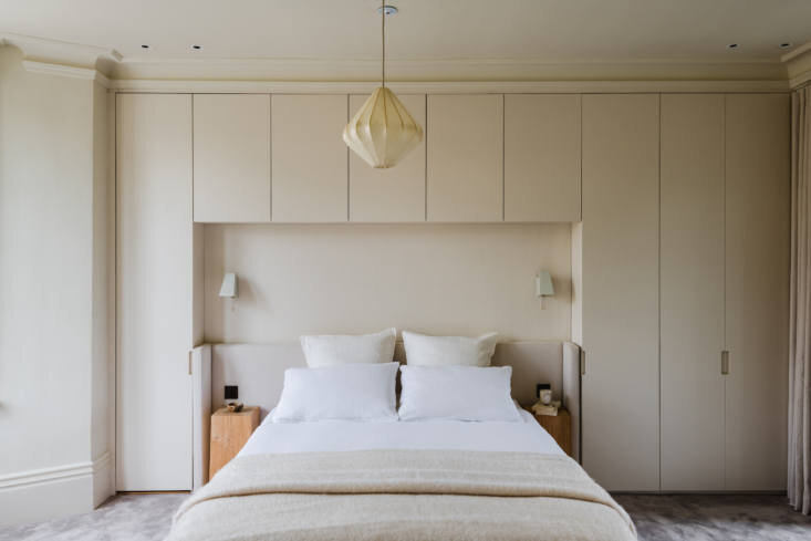 Primary bedroom uses full-height painted wardrobes and a custom bed niche flanked by vintage Scandinavian brass sconces.
