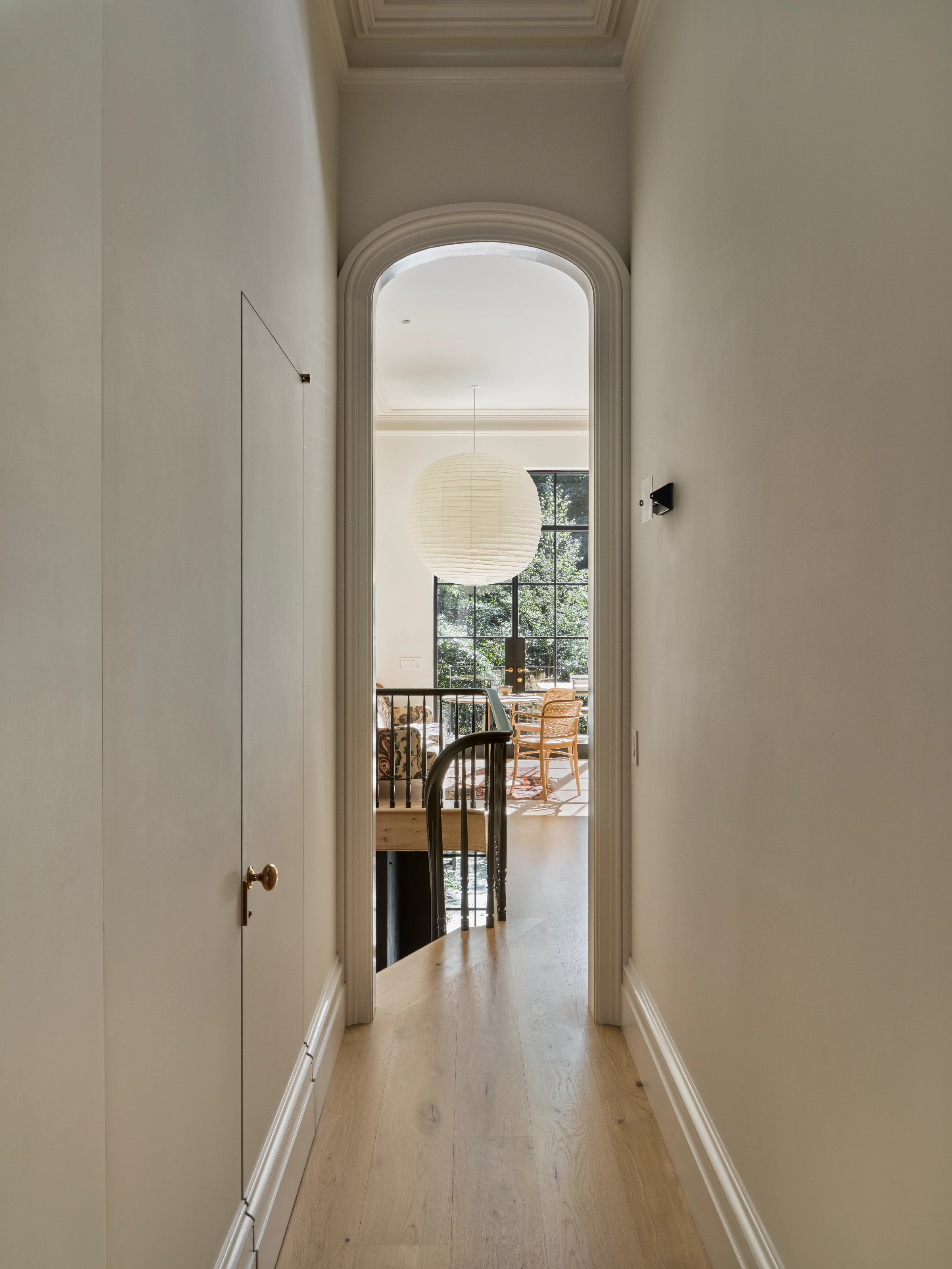 A restored entry sequence uses tall wood casings, pale walls, and a dark runner to re-establish the townhouse's original sense of arrival.