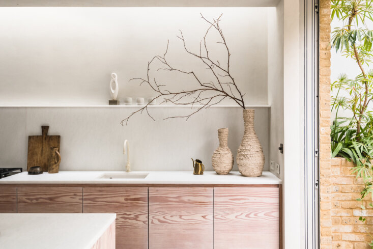 At the sink wall, a powder-coated brass Studio Ore faucet punctuates Evora marble, Douglas fir cabinetry, and branch-filled vessels.