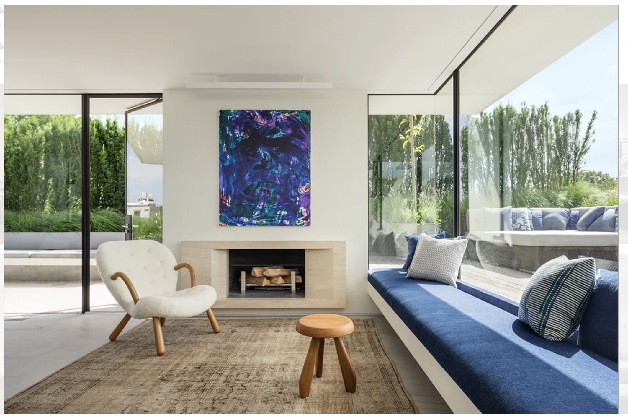 A sitting room with a low fireplace, a built-in blue window bench, and full-height glazing to a planted terrace.
