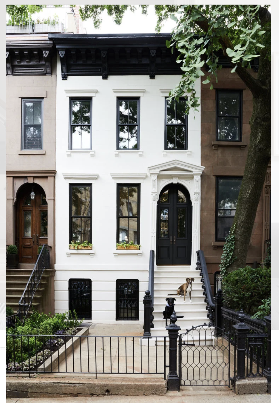 A restored white townhouse facade with black windows, stoop railings, and a dark entry door on a Brooklyn block.